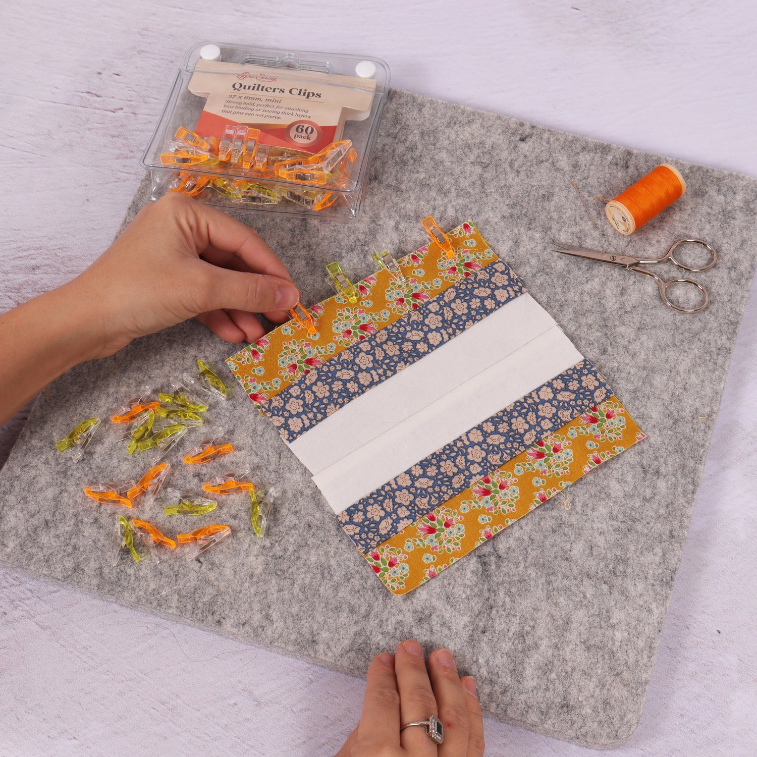 hands sewing a piece of patchwork with thread, scissors and clips