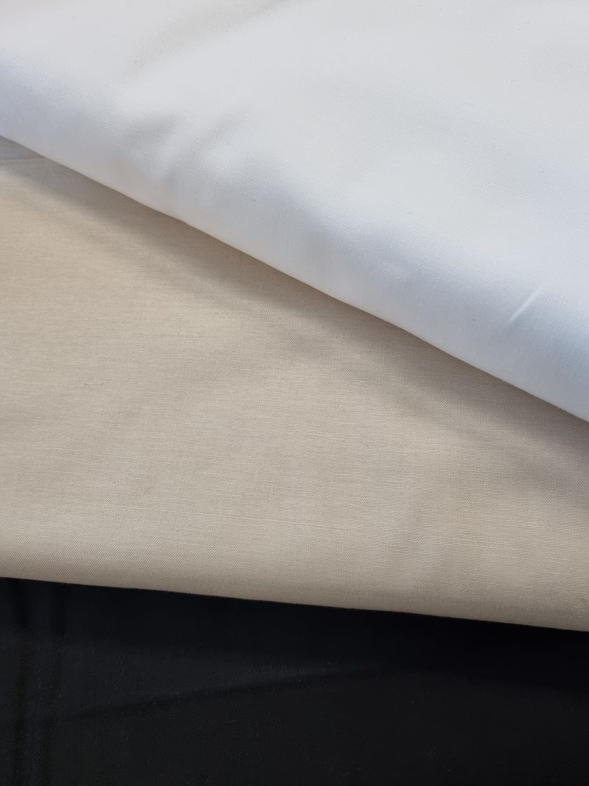 Image shows a roll of off white calico fabric on a brown cardboard inner roll. There are bolts of fabric on a shelf in the background.